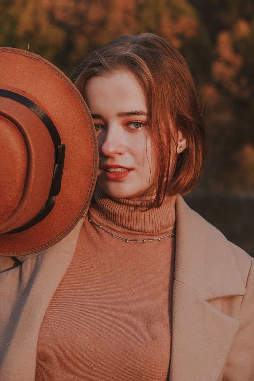 Young woman posing outdoors in fall attire with hat during golden hour.