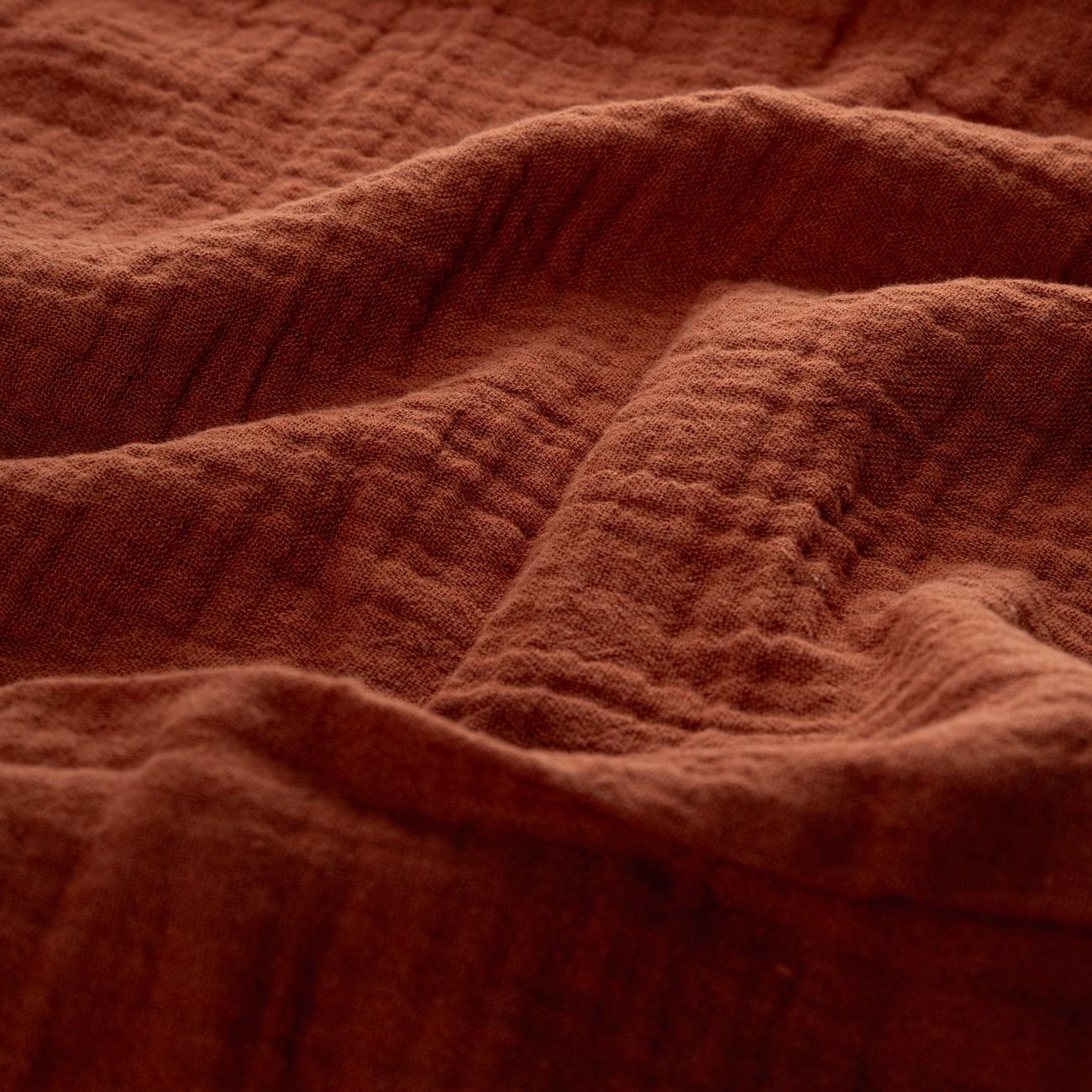 Close-up of warm autumn-colored muslin fabric, showcasing its textured and soft surface.